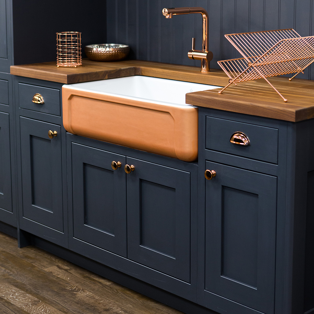 Copper tap and ceramic sink set in a dark blue kitchen unit